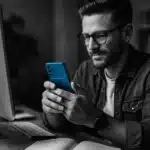 A worker at a desk using a smartphone in a tech-related setting.
