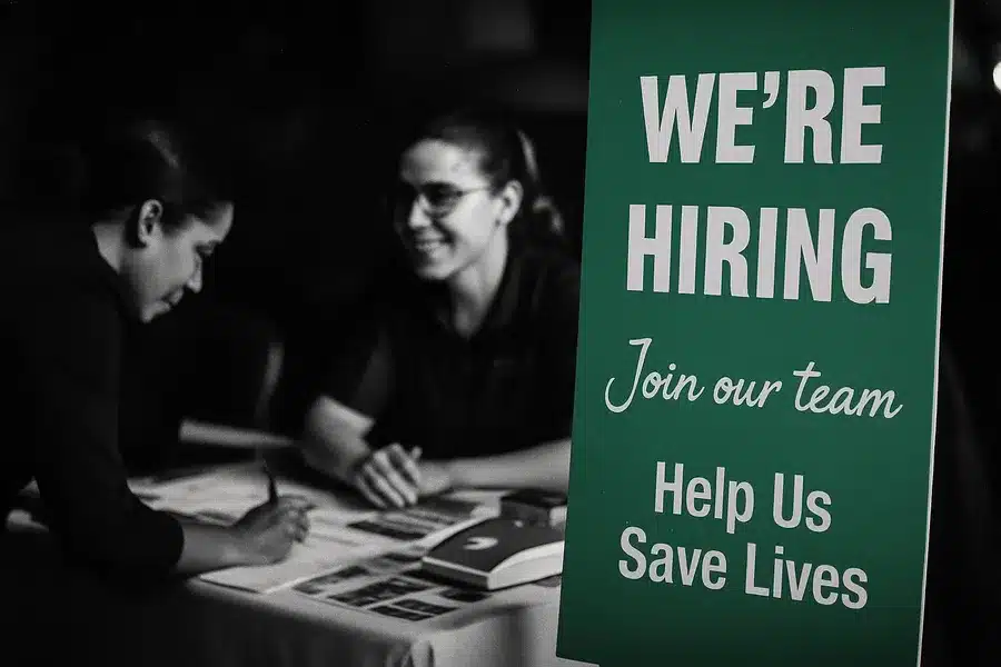 A recruitment booth with 'We're Hiring' signage and two people engaging in conversation.