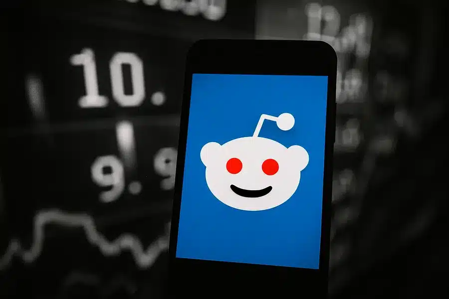 Reddit logo displayed on a smartphone screen in front of stock market graphics.