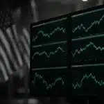 Trading screens displaying financial market data in front of U.S. flags.