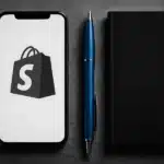 Smartphone displaying the Shopify logo alongside a pen and notebook.